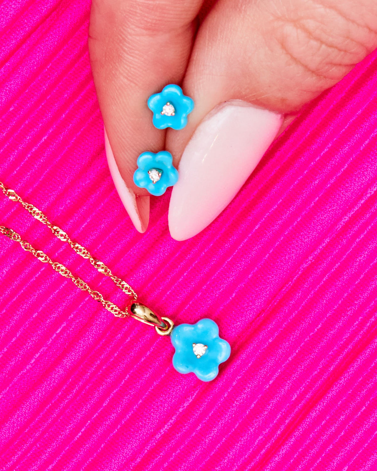 Fingertip holding Diamond Blossom Turquoise Charms on a hot pink background.