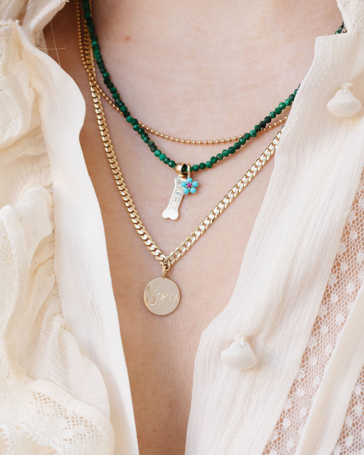Turquoise and Tourmaline Aurora Charm in a layered stack with green beads over a cream ruffled blouse.