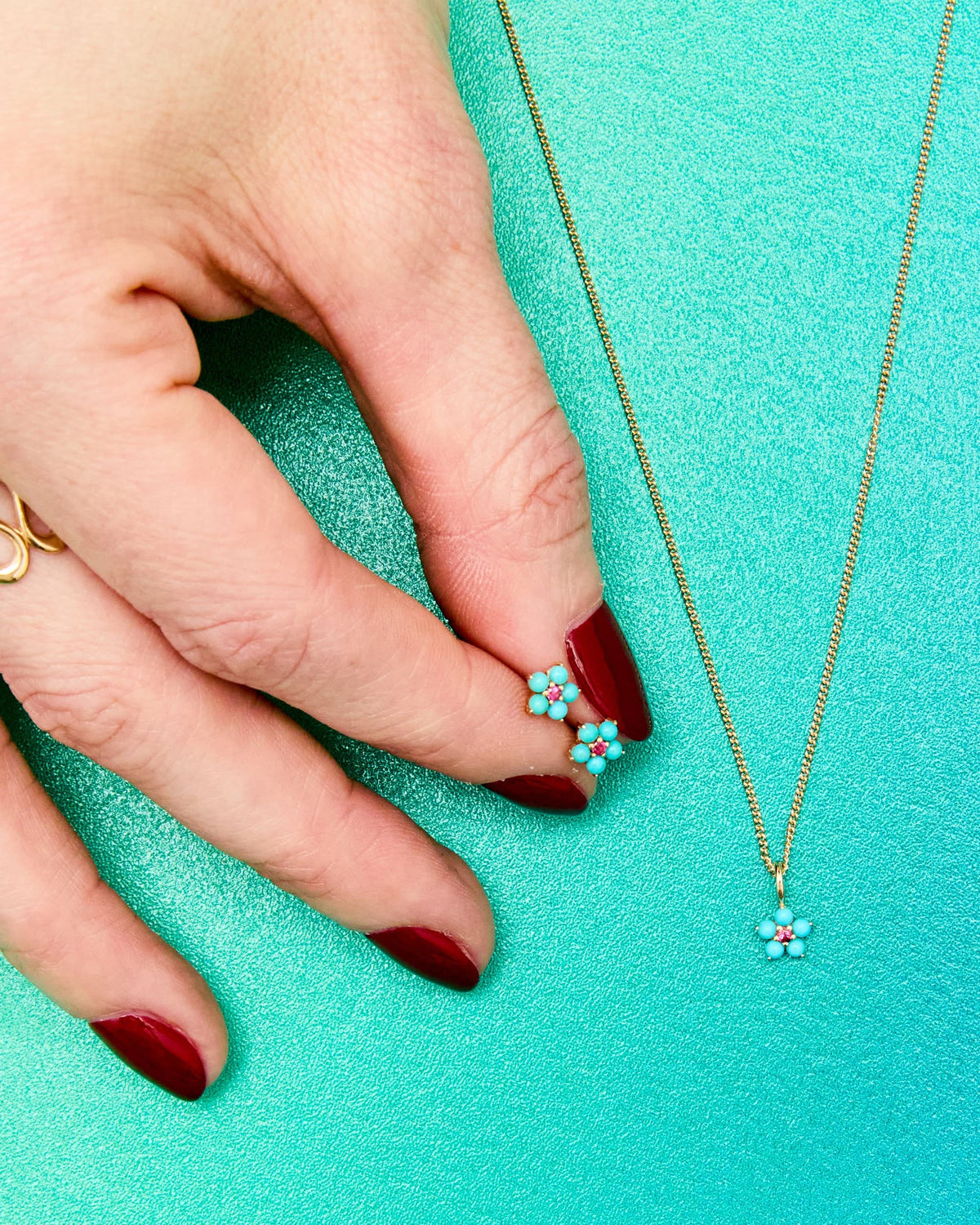 Fingers with red nails holding the Turquoise and Tourmaline Aurora Charm on teal.