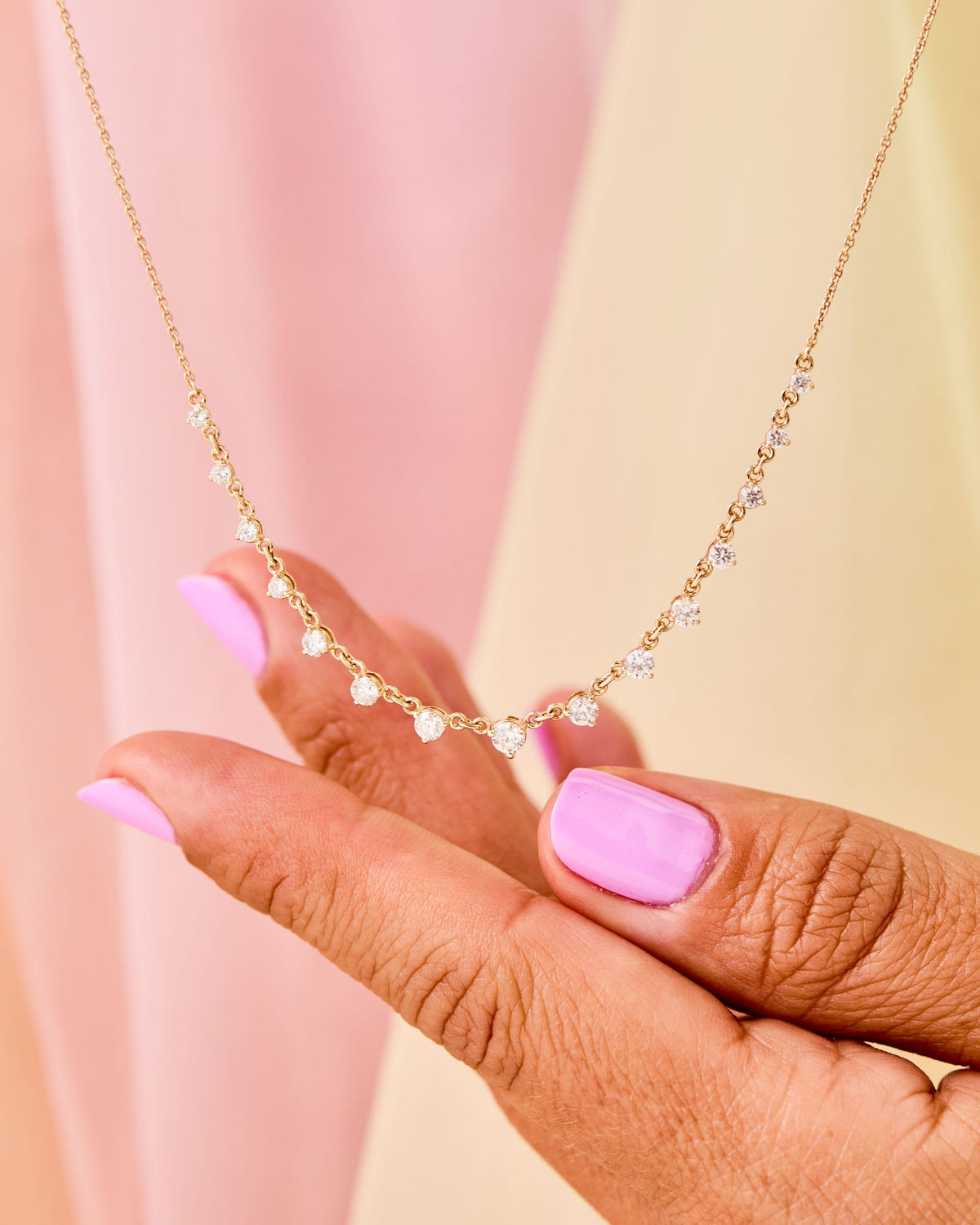 Hand holding the Grande Diamond Cascade Necklace against a pink and yellow curtain.