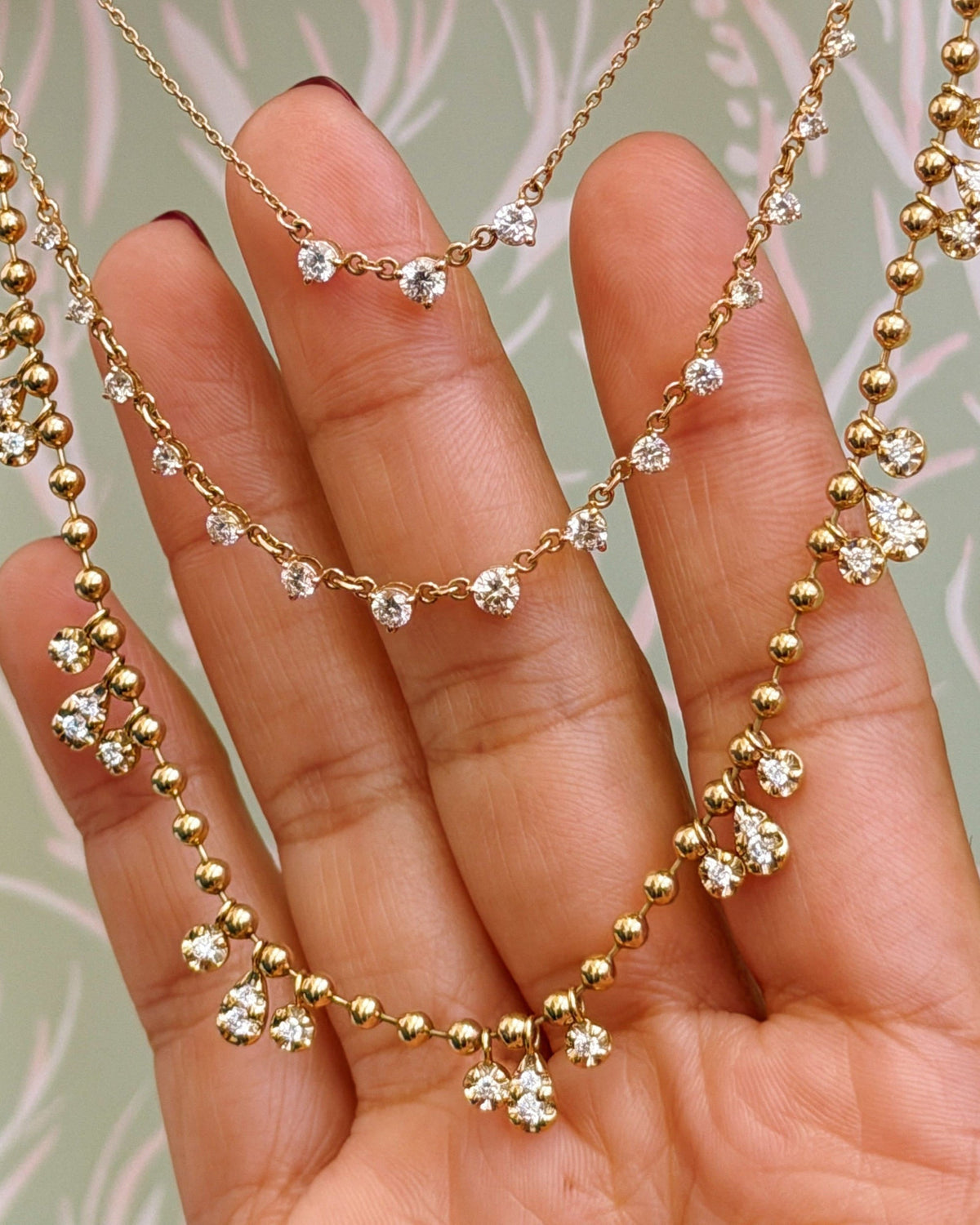 Diamond Cascade necklaces draped over fingers against a green and pink print.