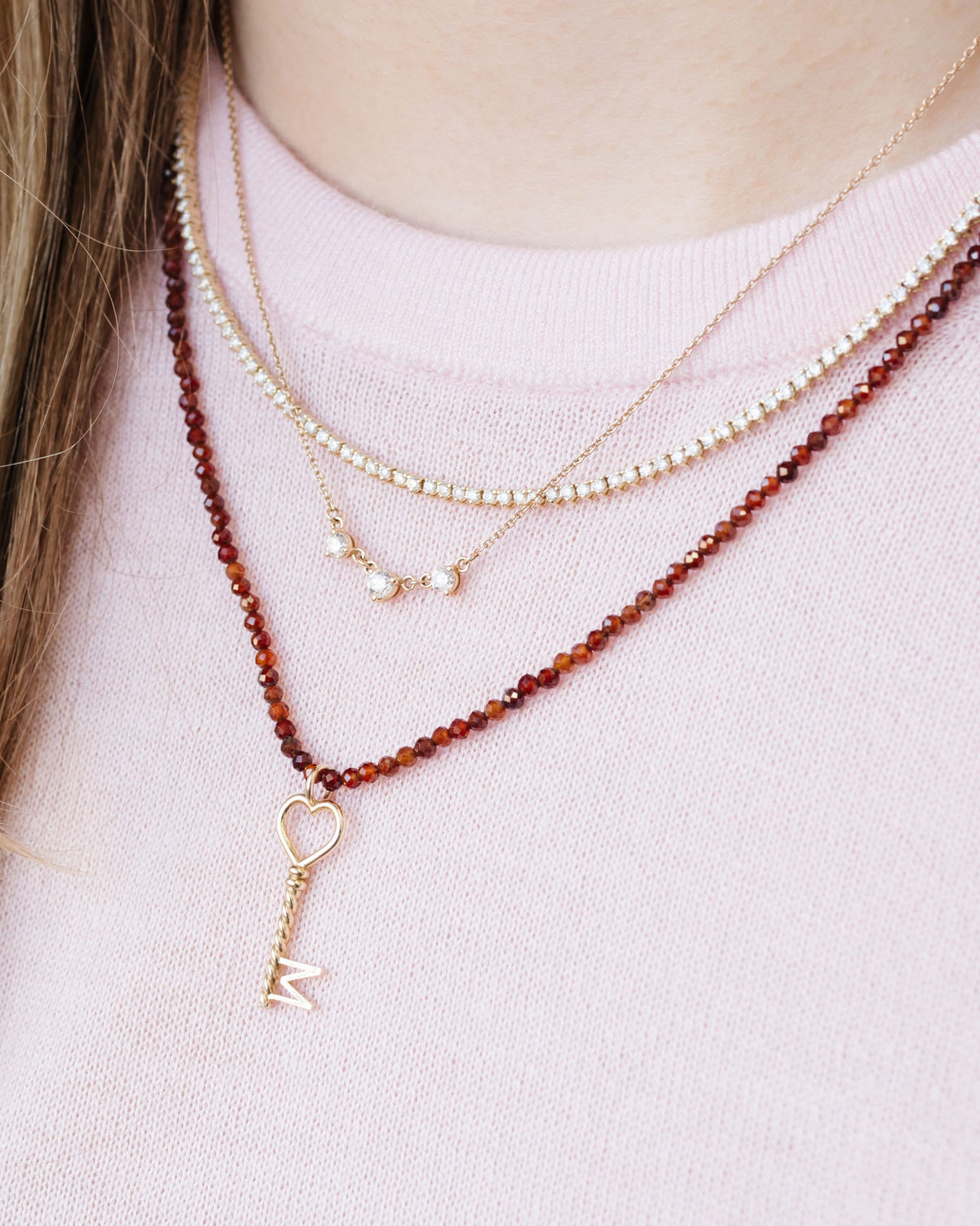 Diamond Cascade Necklace layered with a garnet beaded necklace and a key charm over a pink sweater.