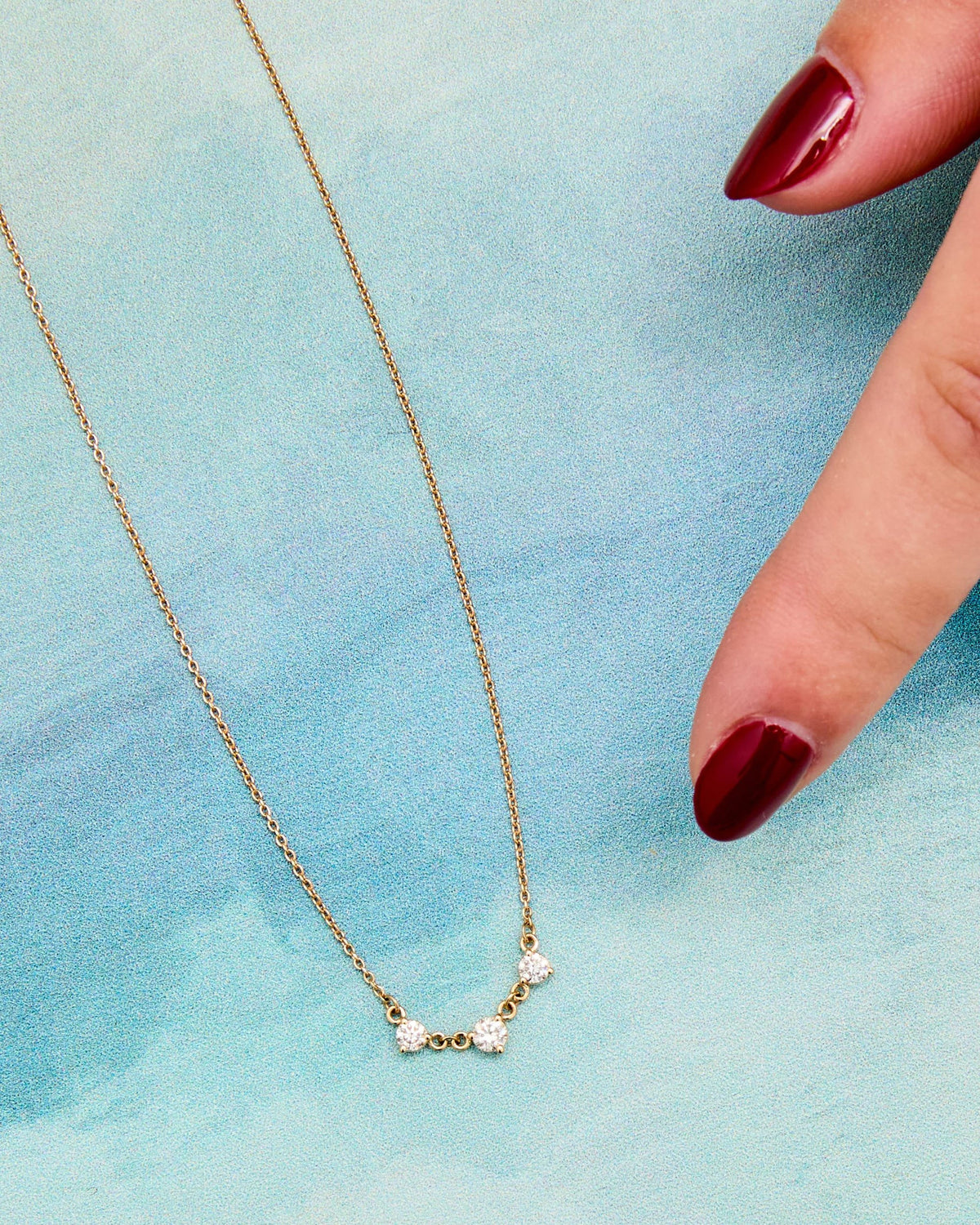 Diamond Cascade Necklace laid on a blue watercolor background, with a fingertip for scale.