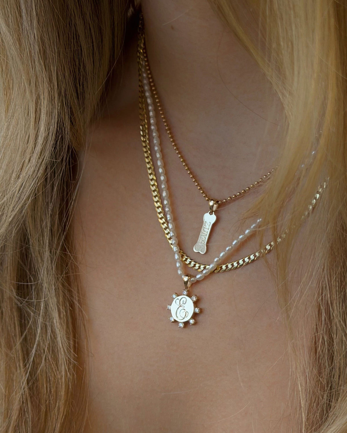 Dog Bone Signet Charm in a layered stack, worn with long blonde hair.