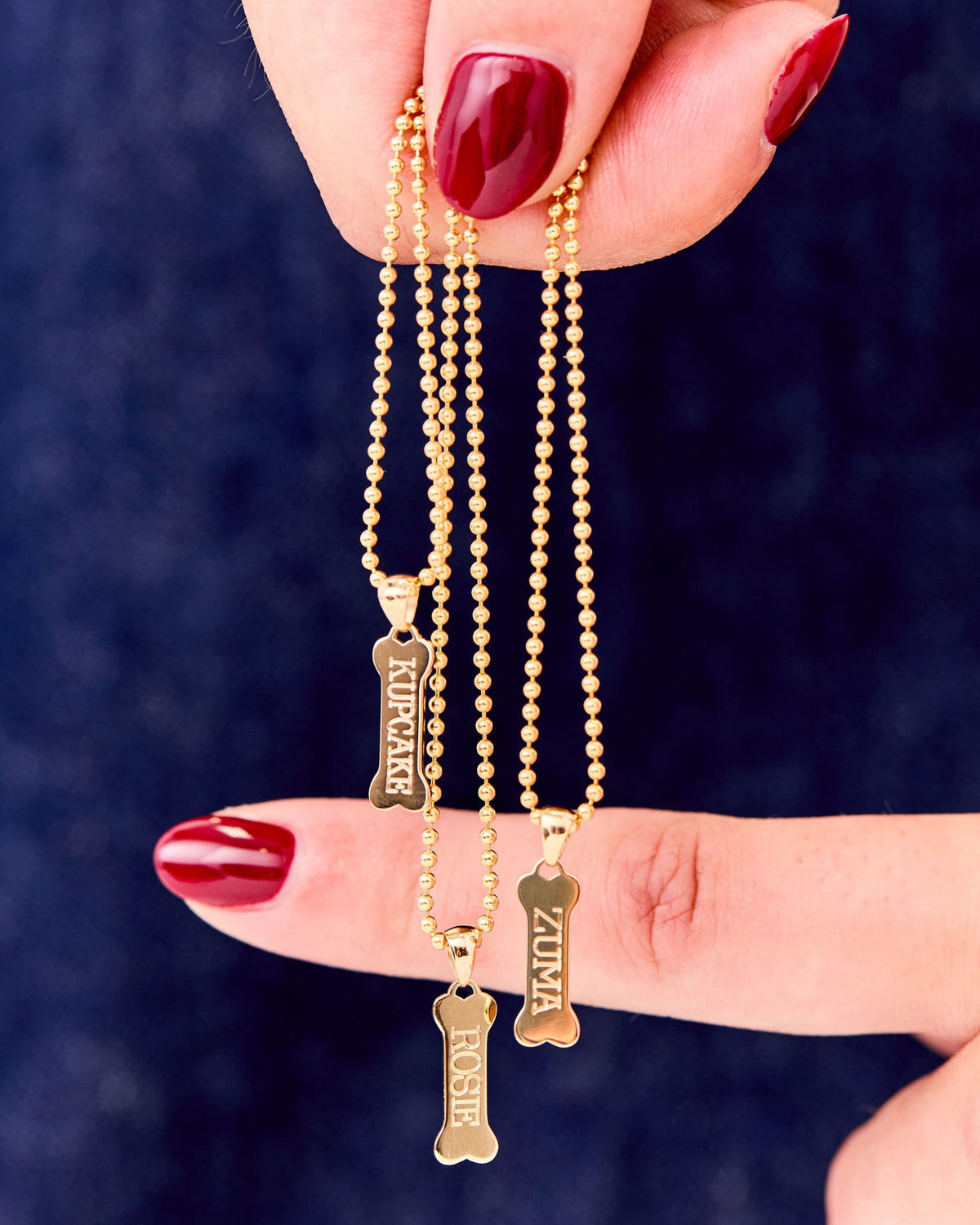 Fingers holding engraved Dog Bone Signet Charms against navy.