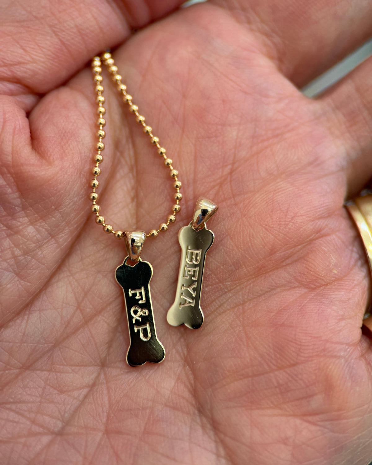 Engraved Dog Bone Signet Charms in an open palm.