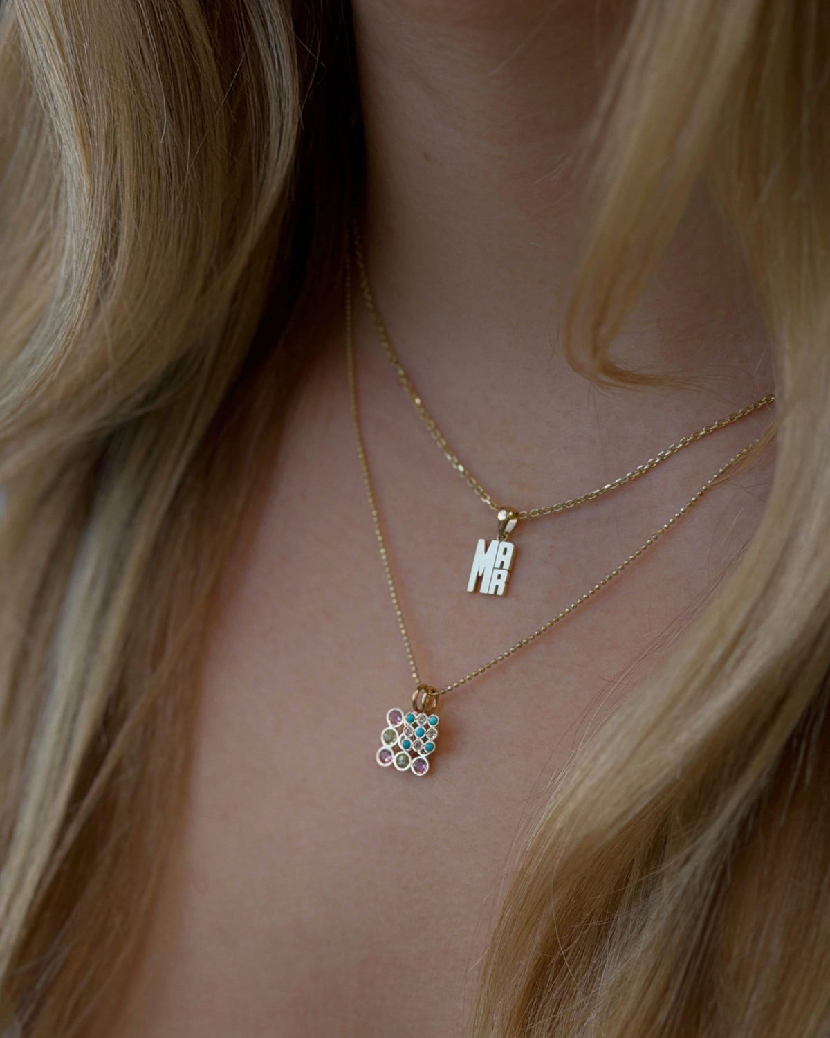 Mini Lucky Strike Monogram Pendant layered with a checkerboard charm, worn with long blonde hair.