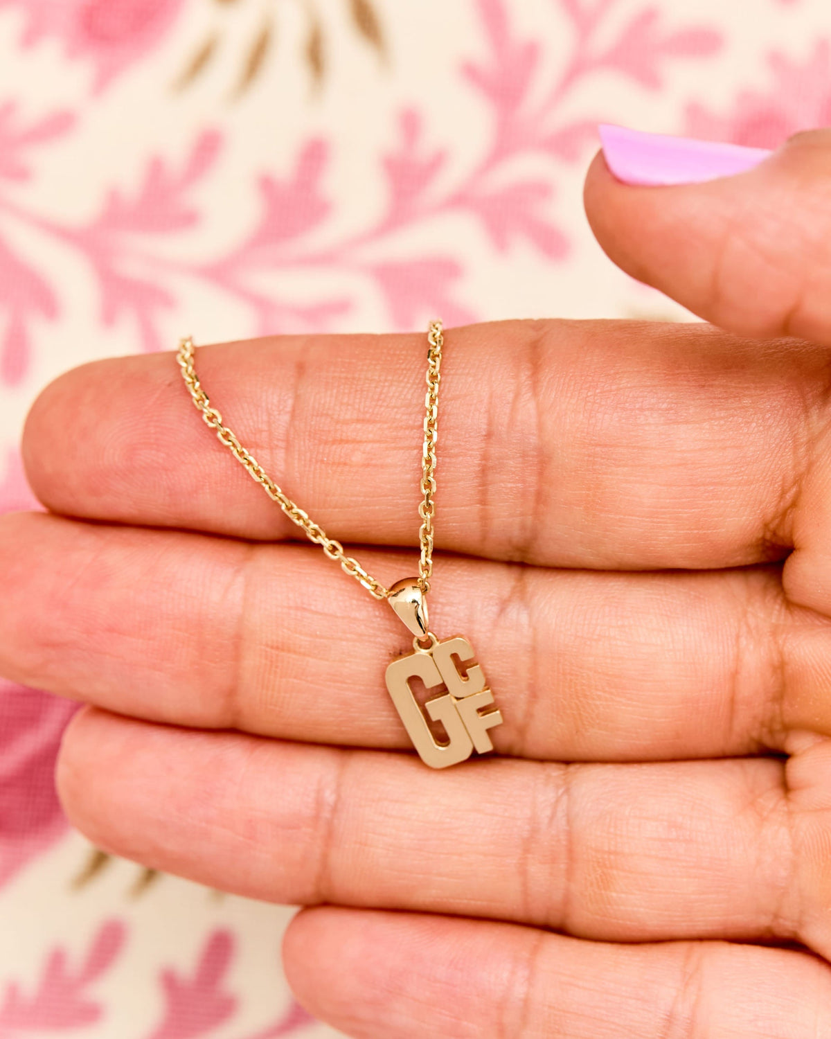 Mini Lucky Strike Monogram Pendant in an open palm on a pink floral print.