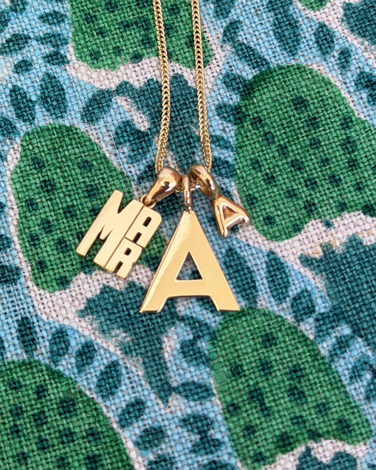 Mini Lucky Strike Monogram Pendant with a letter charm on a green print.