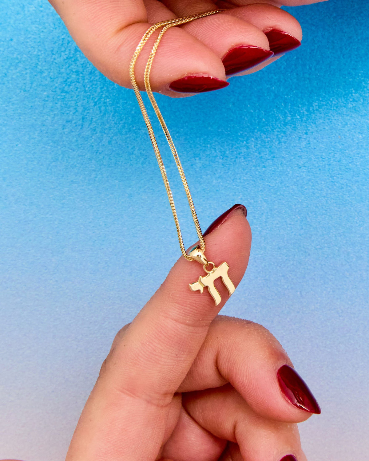 Fingers holding the Chai Talisman Charm against a blue background.