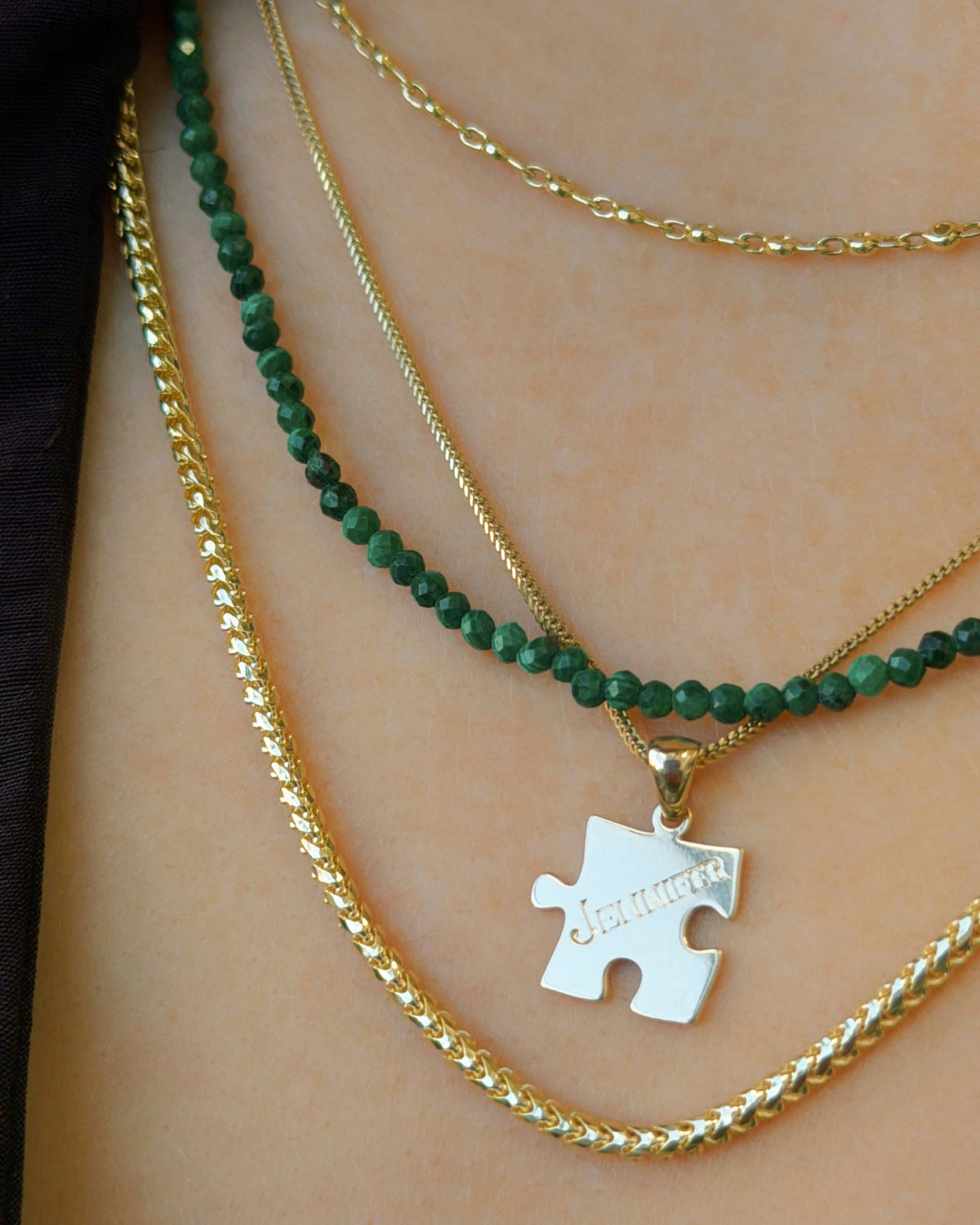 Petite Malachite Beaded Necklace with a puzzle charm, layered with gold chains.