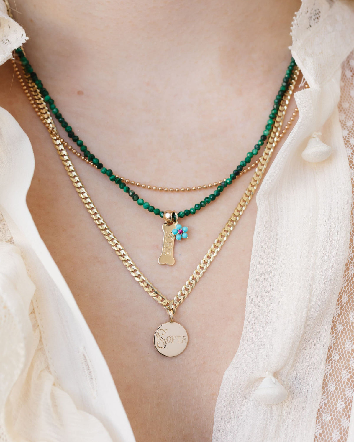 Petite Malachite Beaded Necklace layered with gold chains over a cream ruffled blouse.