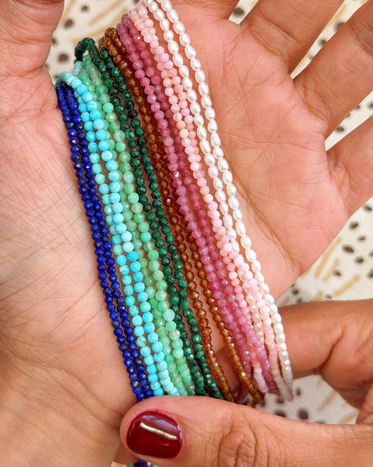 All eight Petite Beaded Necklaces fanned across an open palm, for colour and scale.