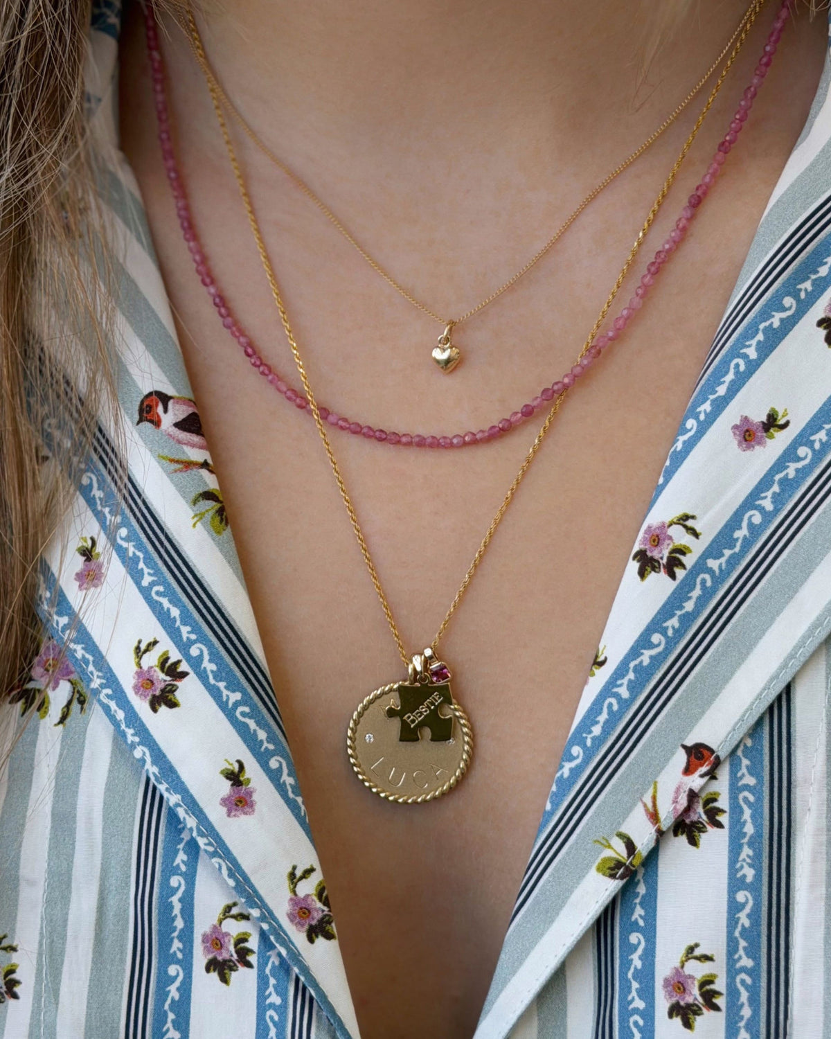 Petite Pink Tourmaline Beaded Necklace layered with a coin pendant over a floral striped shirt.