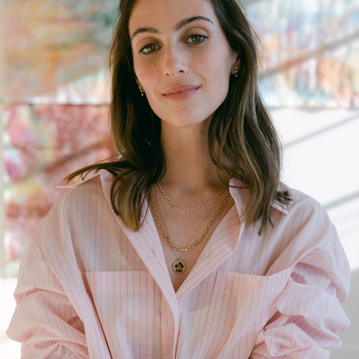 Imperial Portrait Pendant layered with gold chains on a model in an open pink striped shirt.